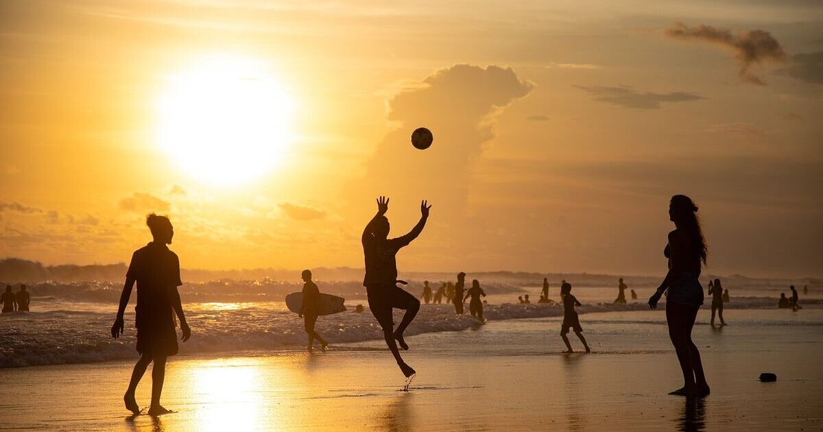 A group playing beach volleyball at sunset